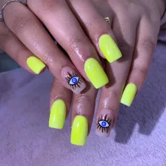 Ward off bad vibes with this trendy evil eye nail art on a bold neon yellow base. The gold glitter details make the design pop.