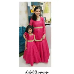 A bright and happy mother-daughter duo in matching pink gowns. The daughter's dress has a cute floral detail on the shoulder.