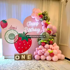 This adorable strawberry-themed first birthday features a large strawberry cutout and a neon "Happy Birthday" sign. The pink and green balloon garland with strawberry accents is a fun, fruity touch.
