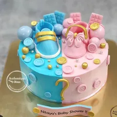 A fun gender reveal cake for a baby shower. This half-pink, half-blue cake is decorated with baby shoes, buttons, and a question mark to build the excitement.