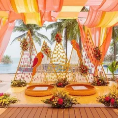 For a beachside mehendi, I designed this vibrant setup with parrot motifs and triangular backdrops. The decor uses a warm color palette of orange and yellow drapes, reflecting the fun and festive mood of a destination wedding.