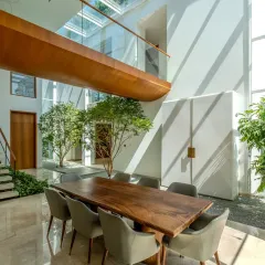 In the double-height dining area of the Split House, a large wooden bridge connects the upper floors. This feature, combined with indoor trees and a massive skylight, blurs the line between inside and out, making the home feel like a part of the landscape.