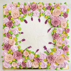 A square cake that serves as a canvas for intricate floral piping. The border is a lush garden of buttercream roses and leaves in shades of pink, purple, and lavender.
