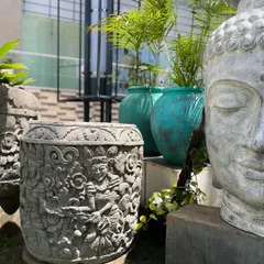 A glimpse of pure bliss. Our intricately carved 'Tara' planter sits beside a serene white Buddha head, a beautiful pairing of artistry and spirituality that elevates any outdoor space.
