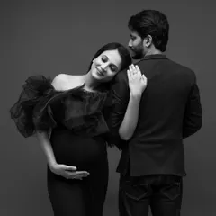 A timeless black and white maternity portrait. The expecting mother, in an elegant black gown, rests her head peacefully on her partner's shoulder, creating a classic and intimate image of their shared anticipation.