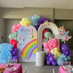 A colorful rainbow unicorn theme for a third birthday. This decor features a double-arched backdrop, a cascade of rainbow-colored balloons, and cute unicorn cutouts.