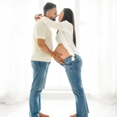 A beautiful silhouette of the couple against a bright, backlit window. This minimalist shot in casual wear focuses on their connection and the lovely shape of the baby bump.