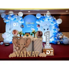 A complete stage setup for Vainav's baby elephant-themed first birthday. The design features a large arched backdrop, balloon garlands, and personalized elements like photo displays and name cutouts.