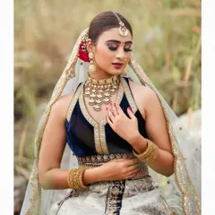An outdoor bridal shoot capturing a serene and elegant moment. The natural setting complements the traditional lehenga, and the soft lighting highlights the delicate details of the fabric and embroidery.