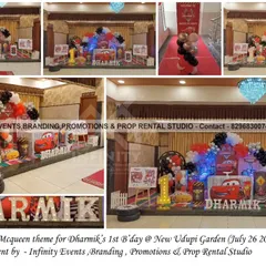 A thrilling Lightning McQueen theme for a first birthday at New Udupi Garden. The decor includes a race track floor mat, character cutouts, and a red, black, and white balloon arrangement.