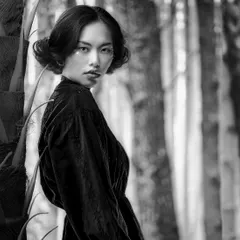 A timeless black and white portrait captured with a projected forest background. The soft lighting and the model's intense gaze create a beautiful fusion of strength and grace.
