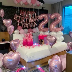 A beautiful pink and rose gold themed bedroom decoration for a 22nd birthday. The setup includes heart-shaped foil balloons, number balloons, and a light-up heart on the floor.