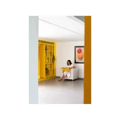 A quiet reading nook within 'The Amber Encase' clubhouse. The vibrant yellow shelving unit acts as both storage and a sculptural element, framing a cozy space for relaxation.
