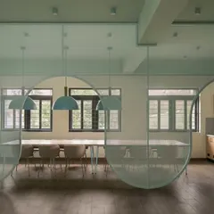 This staff dining area features a translucent, curved partition that creates a sense of separation without closing off the space. The soft green palette and simple wooden furniture create a calming atmosphere for teachers to recharge.