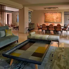 The open-plan design connects the living and dining areas, which were previously separate rooms. A custom-designed coffee table with a patchwork of leather sits at the center, anchoring the space with its unique form.