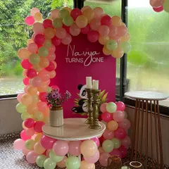 A chic first birthday corner with a balloon arch in shades of pink, peach, and mint green. The custom backdrop features a cute panda graphic for a modern and sweet touch.