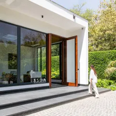 The entrance to The Green Axis office. The design uses large wooden pivot doors and expansive glazing to immediately establish a connection with the lush green hedges and manicured landscape outside.