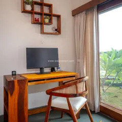 A simple and serene study corner in the Total Environment project, featuring a solid wood desk and chair overlooking a garden, perfect for focused work.