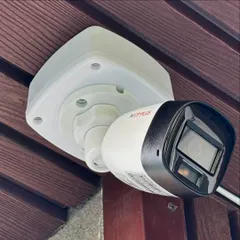 A close-up of a CP Plus 1080p Full HD bullet camera after a neat installation on a wood-paneled balcony ceiling in GK-1. The junction box protects the wiring from weather and ensures a clean, professional finish.
