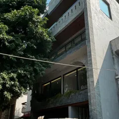 This multi-story residence in West End is nearing completion. The facade features a raw concrete finish, stone cladding, and large arched openings, creating a modern and monumental presence.