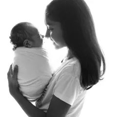A simple and powerful black and white portrait of an older sister holding her newborn sibling. The high-key lighting creates a beautiful silhouette, focusing entirely on their tender interaction.