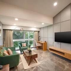 This suite's living area combines comfort and style with plush green sofas, elegant grey wall paneling, and marble-finish flooring. The layout includes a dedicated work desk, making the space versatile for both relaxation and productivity.