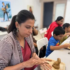 A participant carefully sculpts the fine details of her clay idol, completely absorbed in the mindful and tactile process of creation.