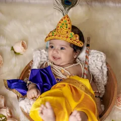 A happy baby Krishna smiling from his basket. We provide all the costumes and props, including the mukut (crown) and pearl necklaces, for a complete and authentic Janmashtami look.