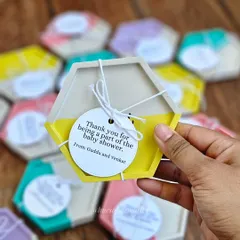 These custom hexagon coasters were made as return gifts for a baby shower. The half-and-half pastel yellow and white design, complete with a personalized tag, makes for a thoughtful and unique party favor.