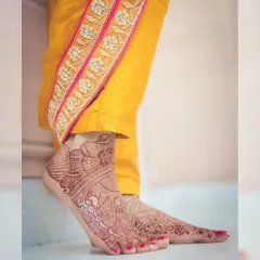An artistic shot focusing on the bride's feet, adorned with detailed mehendi, highlighting the beauty of traditional bridal preparations.
