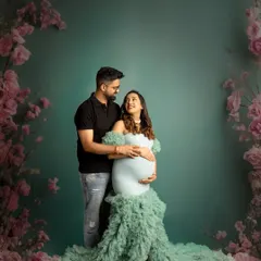 A classic maternity portrait of a couple. They stand together against a beautiful floral backdrop, sharing a look of love and excitement for their journey ahead.