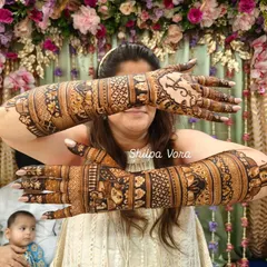 This is how a full bridal design looks when complete, covering the hands and arms in a tapestry of intricate patterns. The bride is joyfully showing off the work.