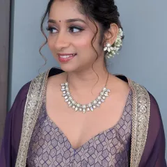 A soft and romantic look for a wedding guest. I used purple tones on the eyes to match her outfit and styled her curly hair into an elegant messy bun with fresh flowers.
