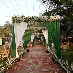 A stunning entrance walkway for a wedding ceremony. The combination of green and white drapes, a floral-printed carpet, and elegant chandeliers creates a grand and welcoming path for guests.