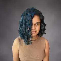 For clients who want to make a statement, I love creating bold, creative looks. I gave Nikita's curly hair an edge with an asymmetrical bob and hand-painted vibrant blue highlights that really pop against her dark hair.