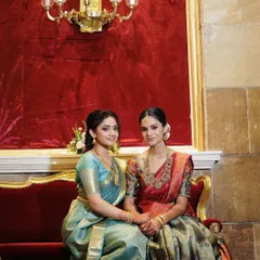 A regal shot of the two sisters at the half saree function. The grand venue and their traditional attire are complemented by elegant, classic makeup.