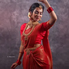 A dynamic pose in a traditional red saree, highlighting the flow and grace of the fabric. This studio shot for a bridal portfolio captures a sense of movement and celebration.