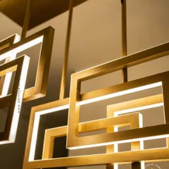 A multi-layered chandelier composed of intersecting rectangular frames with a brushed gold finish. The integrated LEDs cast a warm, ambient light, creating a dynamic and architectural statement piece for modern interiors.
