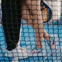 An artistic close-up of the couple's feet and a racket, seen through the court net, focusing on the details of the theme.