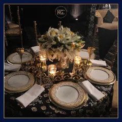 An exquisitely set dining table for a formal event. It features gold-rimmed plates, matching goblets, a beautiful floral centerpiece, and candle lighting, creating an atmosphere of pure opulence.