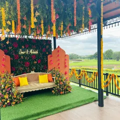 A beautiful outdoor Haldi ceremony with a view. We used a vibrant color palette of orange and yellow with marigold garlands and a lush floral wall backdrop to create a cheerful and picturesque setting.