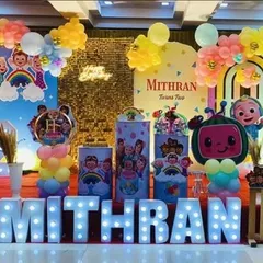 A vibrant Cocomelon party with a gold sequin backdrop and large marquee letters. The setup is filled with character cutouts and colorful balloon arrangements.