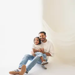 A relaxed and happy portrait of a father and daughter. The simple white background and matching casual outfits keep the focus entirely on their wonderful connection.