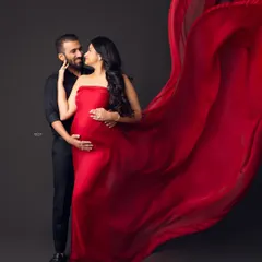 Power and passion in one frame. A bold red tossing fabric creates a sense of movement and drama around the couple, highlighting the mother's glowing profile in this captivating maternity portrait.