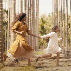 A dynamic shot from the music video 'MANNIPU'. The costumes, a mustard yellow kurta and a simple white dress, were designed with light, natural fabrics to create beautiful movement as the artists run through the betel nut farm.