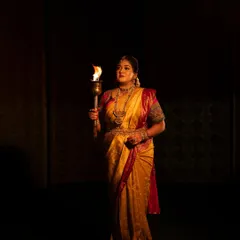 A full-length shot from the "Belaku" concept, showing the subject holding the torch in a powerful stance. The low-light photography creates a mystical and intense atmosphere.