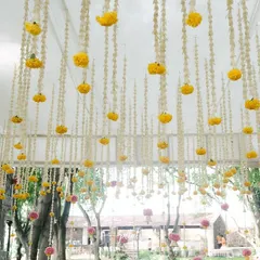 A beautiful ceiling installation for a traditional wedding, featuring hanging strings of yellow marigolds and white tuberoses. This floral canopy transforms the space and adds a festive touch.