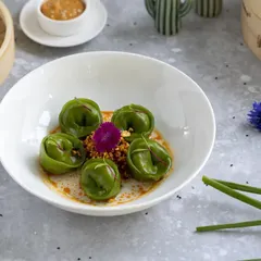 This is an example of modern, artistic food plating. The vibrant green of the spinach dumplings pops against the clean white bowl, while the careful placement of garnishes highlights the dish's elegance for a fine-dining menu.