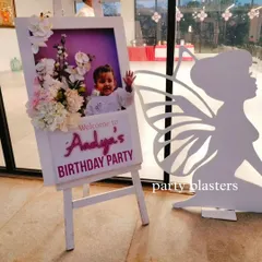 We create personalized welcome easels for our events. This one for Aadya's party features a photo of the birthday girl, custom text, and is decorated with a fairy cutout and flowers.