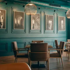 The dining room at Salt and Cravings features deep teal walls with classic molding, creating a sophisticated backdrop for the black-and-white architectural photography. The warm wood tones of the furniture provide a pleasing contrast.